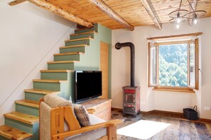A wooden staircase with a flat-screen TV on a wooden console, a fireplace, and a window with a view of trees.
