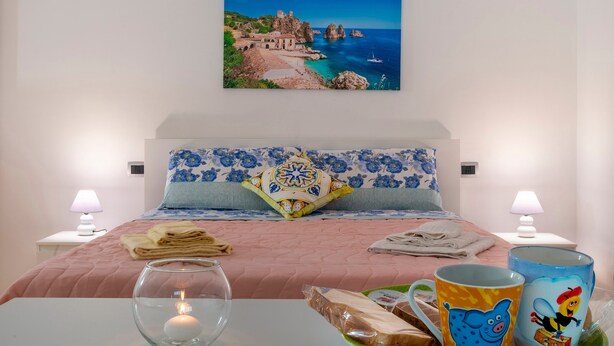 Ein Schlafzimmer mit einem Bett, einem Nachttisch mit Lampe, einem Glas Wasser, einem Teller mit Brot und einer Tasse mit einer Zeichentrickfigur.