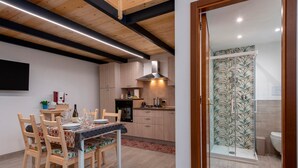 Eine moderne Küche mit Holzausstattung, einem Esstisch mit Stühlen und einer Dusche mit Musterfliesen.