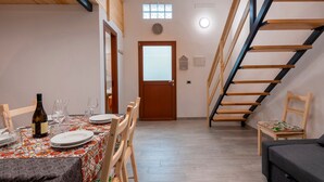 Ein Essbereich mit einem Tisch für zwei Personen, einer Weinflasche und einem Sessel mit Kissen. Eine Treppe ist rechts im Bild zu sehen.