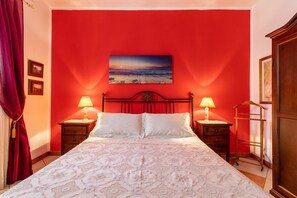 A bedroom with a red wall, a bed with white bedding, two bedside lamps, and a painting above the bed.