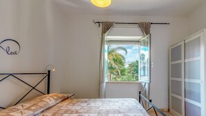 Une chambre à coucher avec un lit, une fenêtre avec des rideaux, une vue sur la verdure et une armoire.