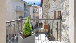 Un balcone con un vaso di alberi, un muro in pietra e vista su una stretta via con edifici.