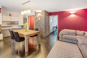Un salon moderne comprenant un canapé, une table à manger avec des chaises et un coin cuisine avec des placards et un mur d’accent en pierre.