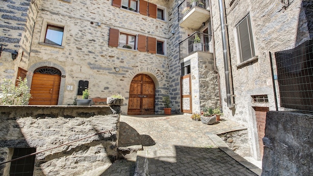 Un edificio in pietra con porte e finestre in legno, una scala in pietra e un piccolo cortile.