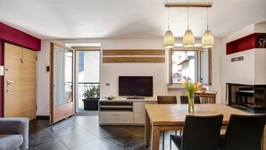 Un soggiorno moderno con TV, tavolo da pranzo in legno, sedie, camino e un balcone con vista.