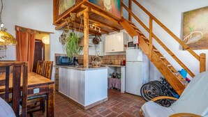 Una cocina con isla central, escalera de madera y comedor con sillas.