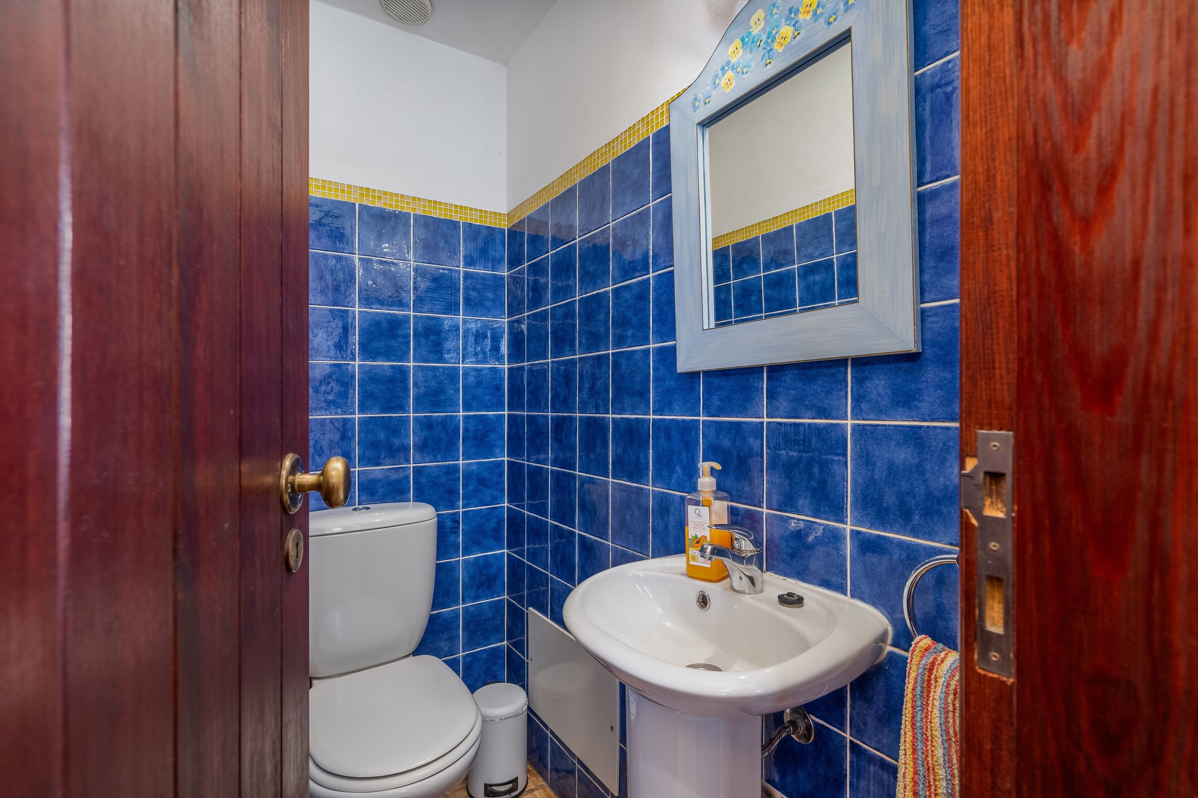 Ein Badezimmer mit blauen Fliesen, einem weißen Waschbecken, einem Spiegel und einer Holztür.