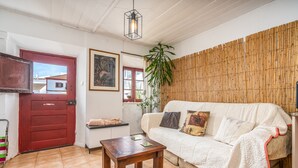 A cozy living room with a red door, a white sofa, a wooden table, and a large plant. - Holiday Home "Casa da Praia 2" with Sea View, Terrace & Wi-Fi (Budens)