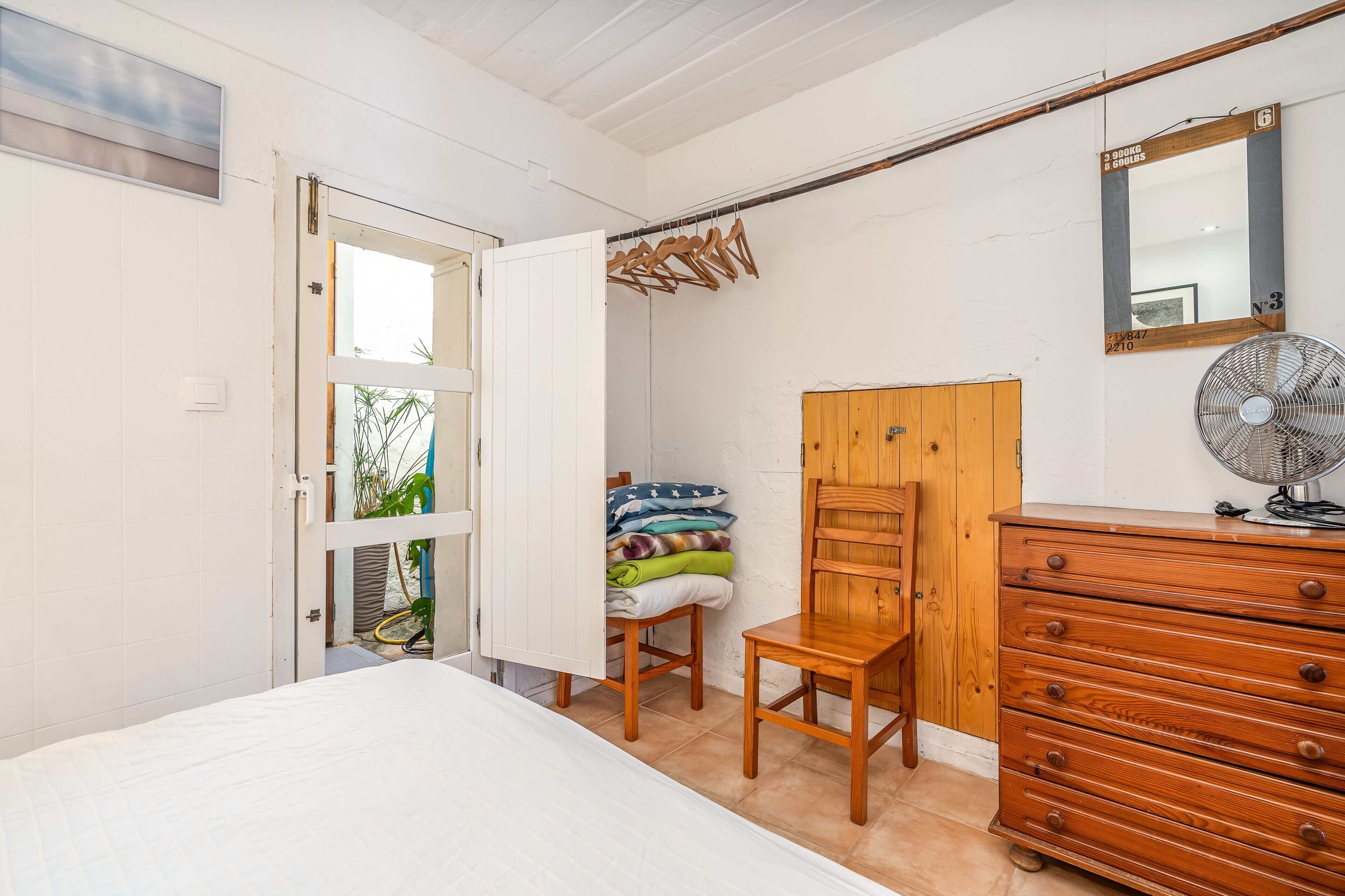 Een slaapkamer met een bed, een houten dressoir en een ventilator.
