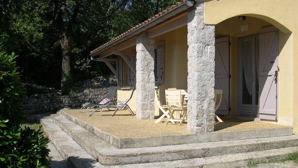 Un edificio revestido de piedra con un porche cubierto, mesas al aire libre y una escalera de piedra que conduce a la entrada.