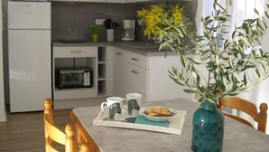 Una cocina compacta con gabinetes blancos, microondas, tostadora y cafetera. Hay una mesa con una bandeja que contiene galletas y dos tazas con estampado de cebra. Un jarrón con flores amarillas está sobre la mesa.
