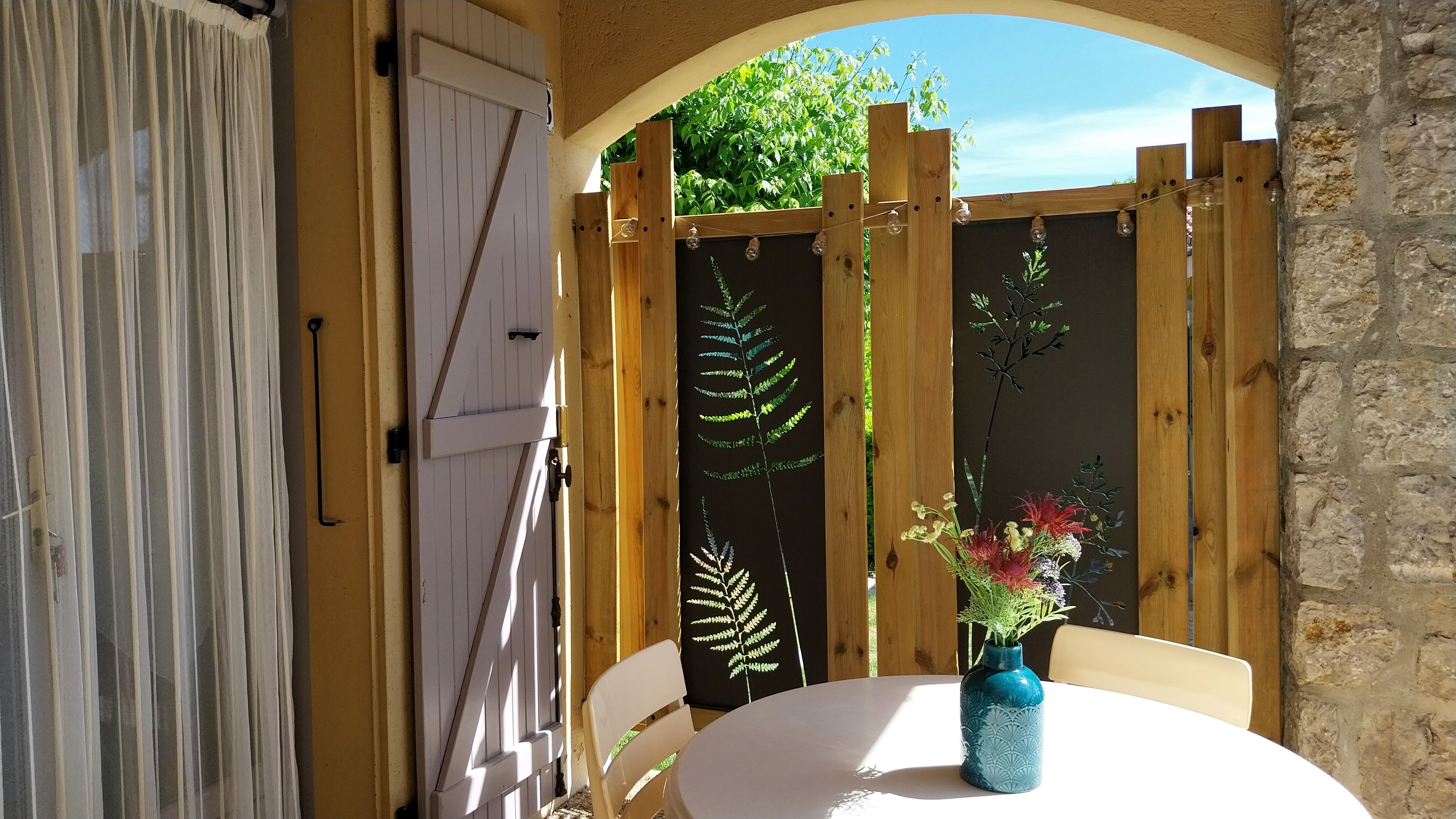 An outdoor seating area with a table, chairs, and a vase with flowers.