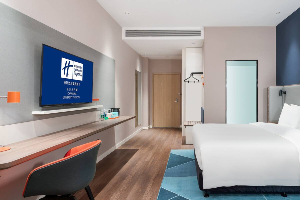 A hotel room with a bed, a desk with a chair, a TV on the wall, and a wardrobe.