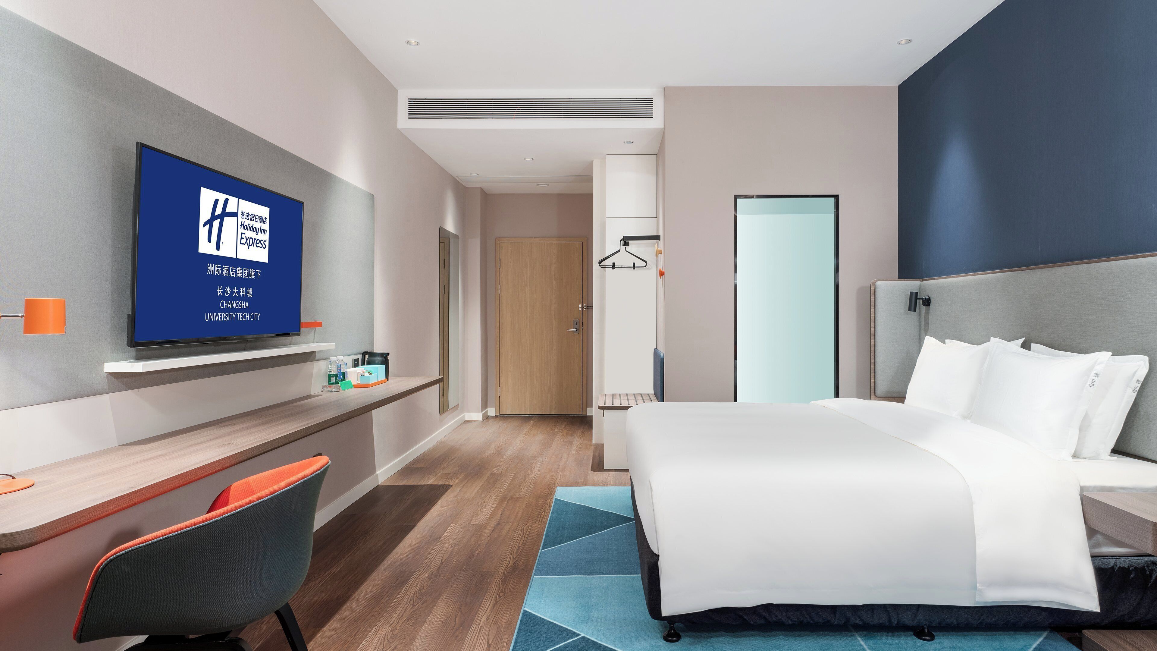 A hotel room with a bed, a desk, a chair, a TV, and a wardrobe.