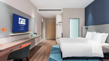A hotel room with a bed, a desk, a chair, a TV, and a wardrobe.