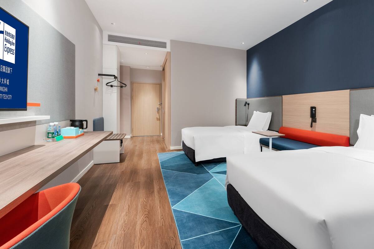 A hotel room with two beds, a desk, and a seating area.