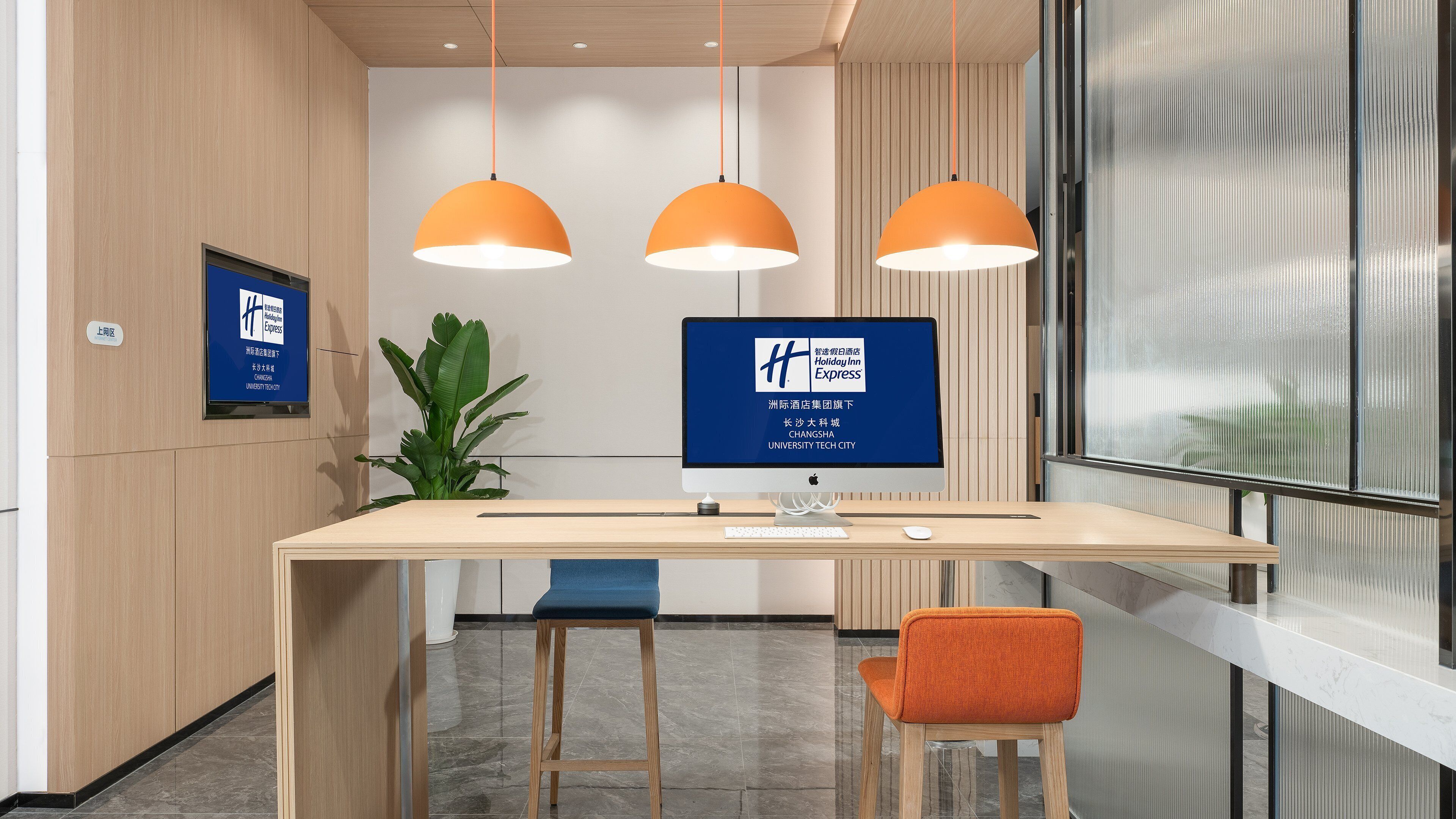 A modern reception desk with a computer monitor, a plant, and two chairs.
