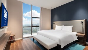 A modern hotel room with a large bed, a bedside table, a TV on the wall, and a view of the city through large windows. - Holiday Inn Express Changsha University Tech City by IHG (Changsha)