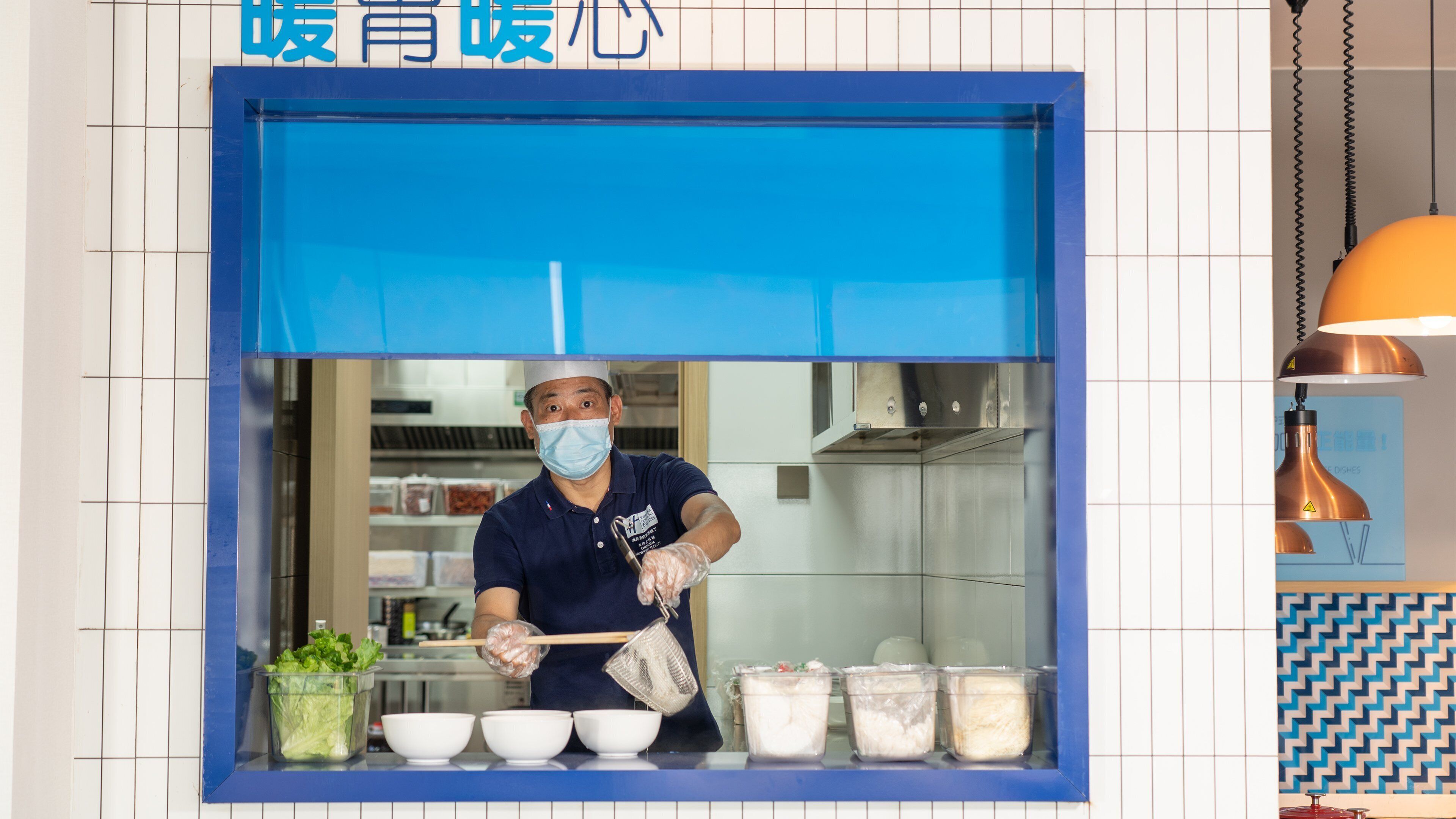 Una cocina con mostrador azul, una persona cocinando y diversos utensilios e ingredientes.
