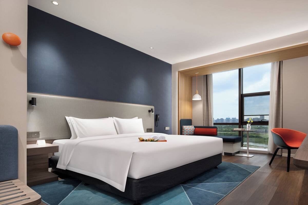 A modern hotel room with a large bed, a desk, and a view of the city.