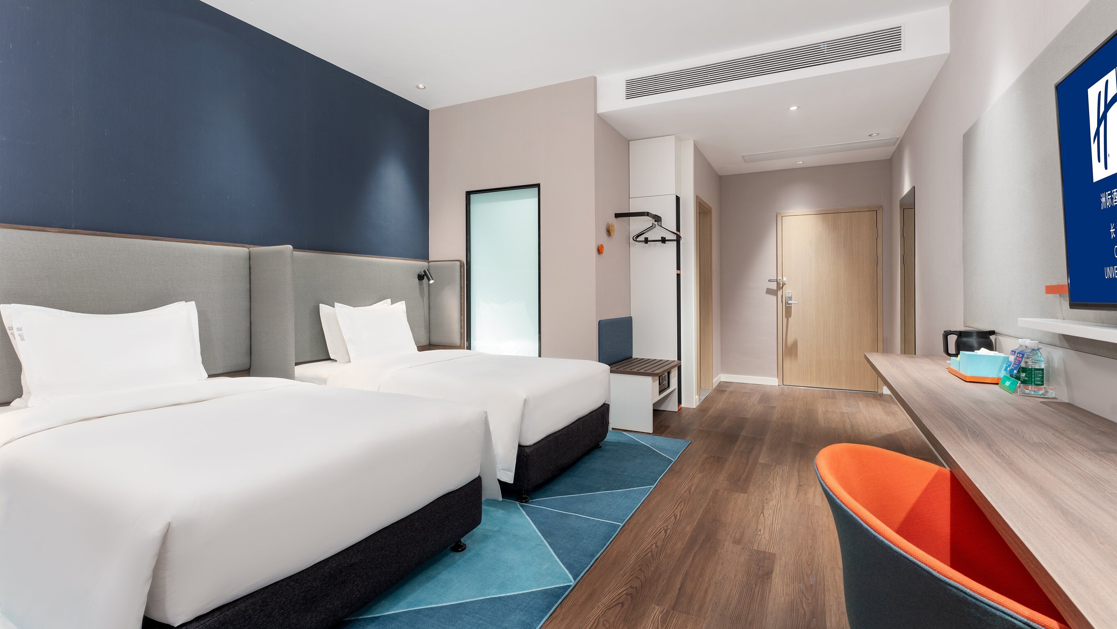 A hotel room with two beds, a desk, a chair, and a bathroom door.