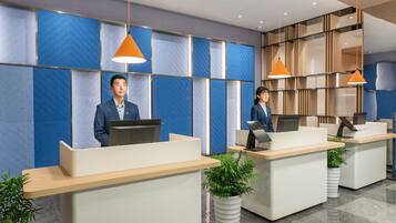 A modern reception area with two receptionists, blue patterned walls, wooden shelves, and potted plants.