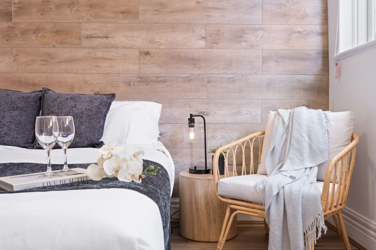 A bedroom with a bed, two bedside tables, a chair, a lamp, and a window.