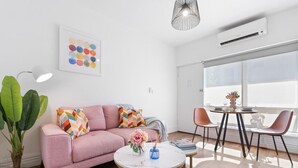 A modern living room with a pink sofa, a round coffee table, and a dining area with two chairs. - Hidden Cozy Gem In Caulfield North (Caulfield North)