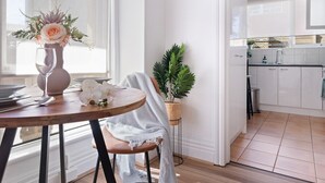 A modern kitchen with white cabinets, a wooden dining table with a vase of flowers, and a potted plant. - Hidden Cozy Gem In Caulfield North (Caulfield North)