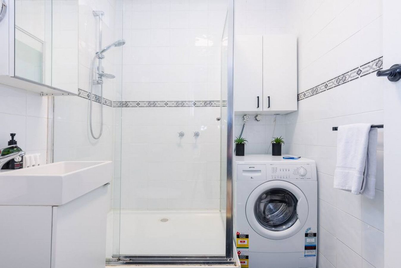 A modern bathroom with a glass-enclosed shower, a sink, a washing machine, and a cabinet.