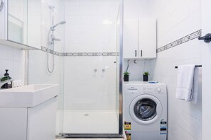 A modern bathroom with a glass-enclosed shower, a sink, a washing machine, and a cabinet. - Hidden Cozy Gem In Caulfield North (Caulfield North)