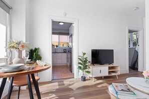 A modern living room with a dining area, a television, and a kitchen in the background. - Hidden Cozy Gem In Caulfield North (Caulfield North)