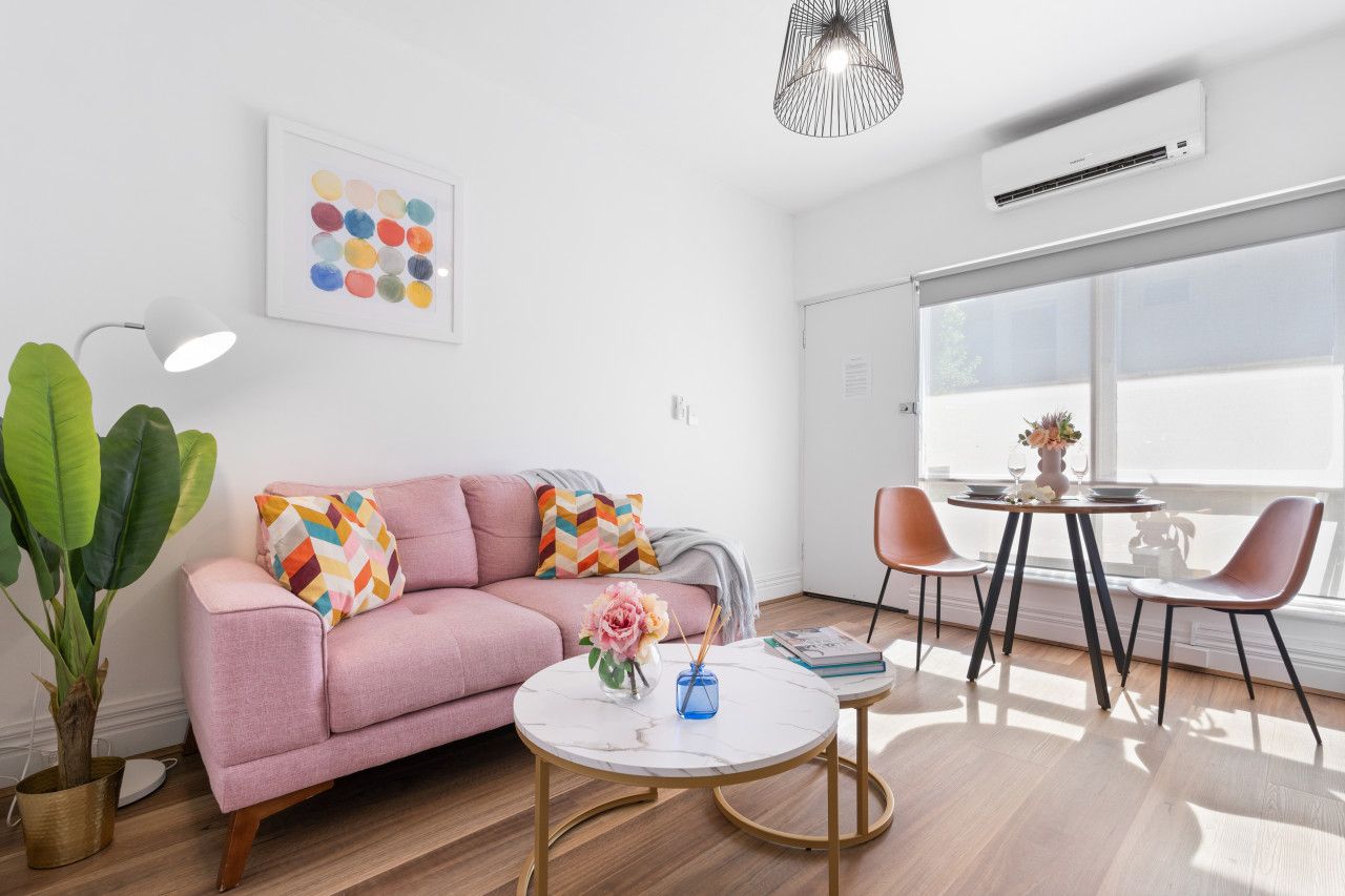 A modern living room with a pink sofa, a round coffee table, and a dining area with two chairs.