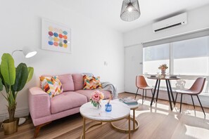 A modern living room with a pink sofa, a round coffee table, and a dining area with two chairs. - Hidden Cozy Gem In Caulfield North (Caulfield North)