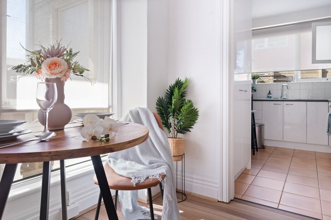 A modern kitchen with white cabinets, a dining area with a table set for two, and a potted plant.