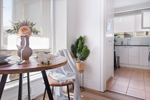 A modern kitchen with white cabinets, a dining area with a table set for two, and a potted plant. - Hidden Cozy Gem In Caulfield North (Caulfield North)