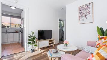 A modern living room with a flat-screen TV, a sofa, a coffee table, and a potted plant.