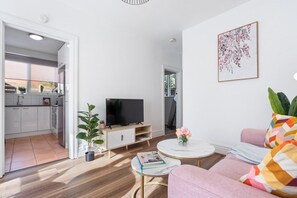 A modern living room with a flat-screen TV, a sofa, a coffee table, and a potted plant. - Hidden Cozy Gem In Caulfield North (Caulfield North)