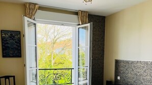 Una camera da letto con due letti, una finestra con tende, una sedia e un quadro appeso al muro.