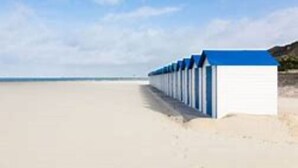 Una fila di cabine sulla spiaggia, con una spiaggia sabbiosa e l'oceano sullo sfondo.