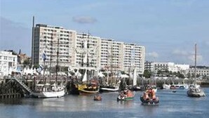 Un hotel sul lungomare con diversi piani, un molo con barche e cielo sereno.
