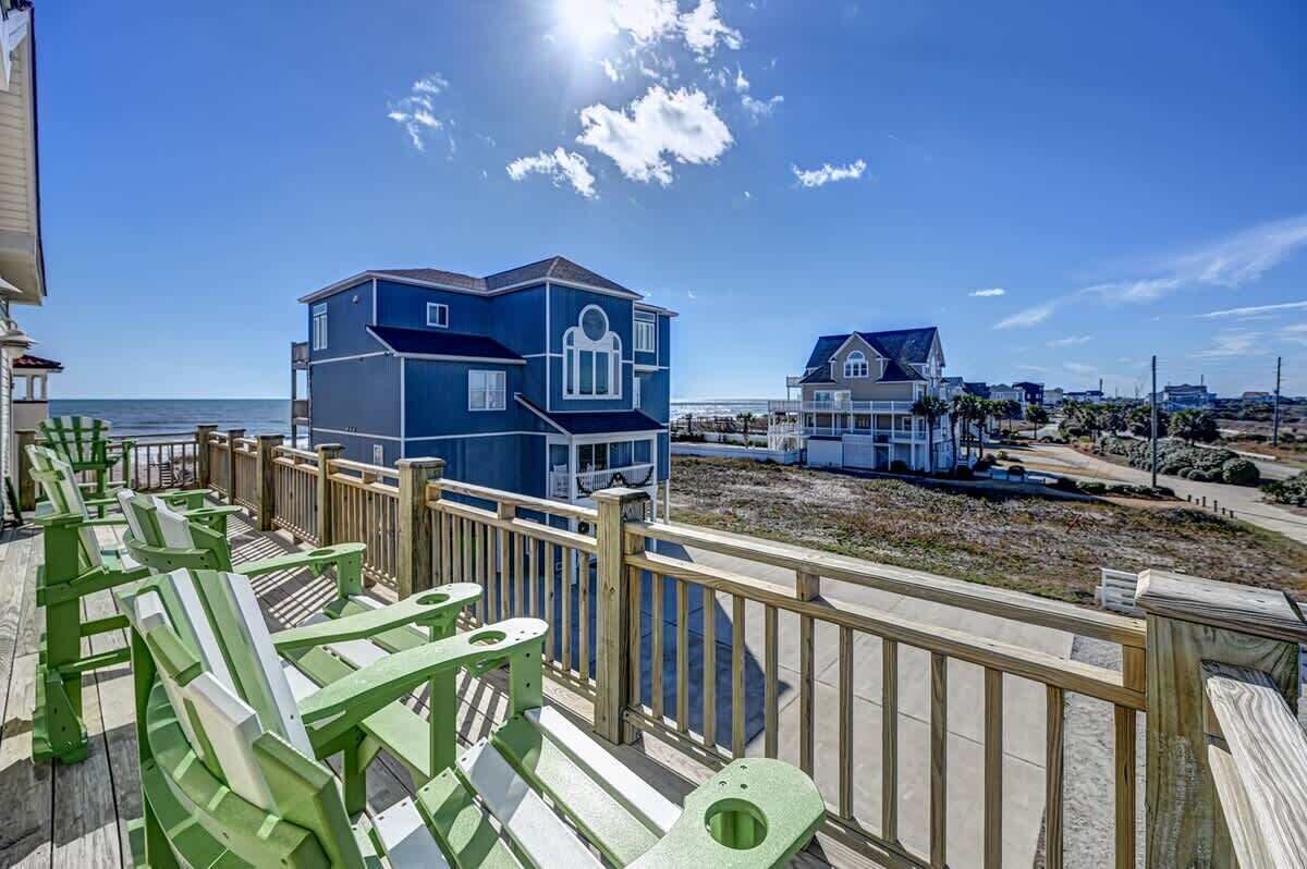 Una proprietà sul lungomare con una grande casa blu, una più piccola e un molo di legno con sedie verdi.