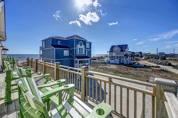 A beachside property with a large blue house, a smaller house, and a wooden deck with green chairs.