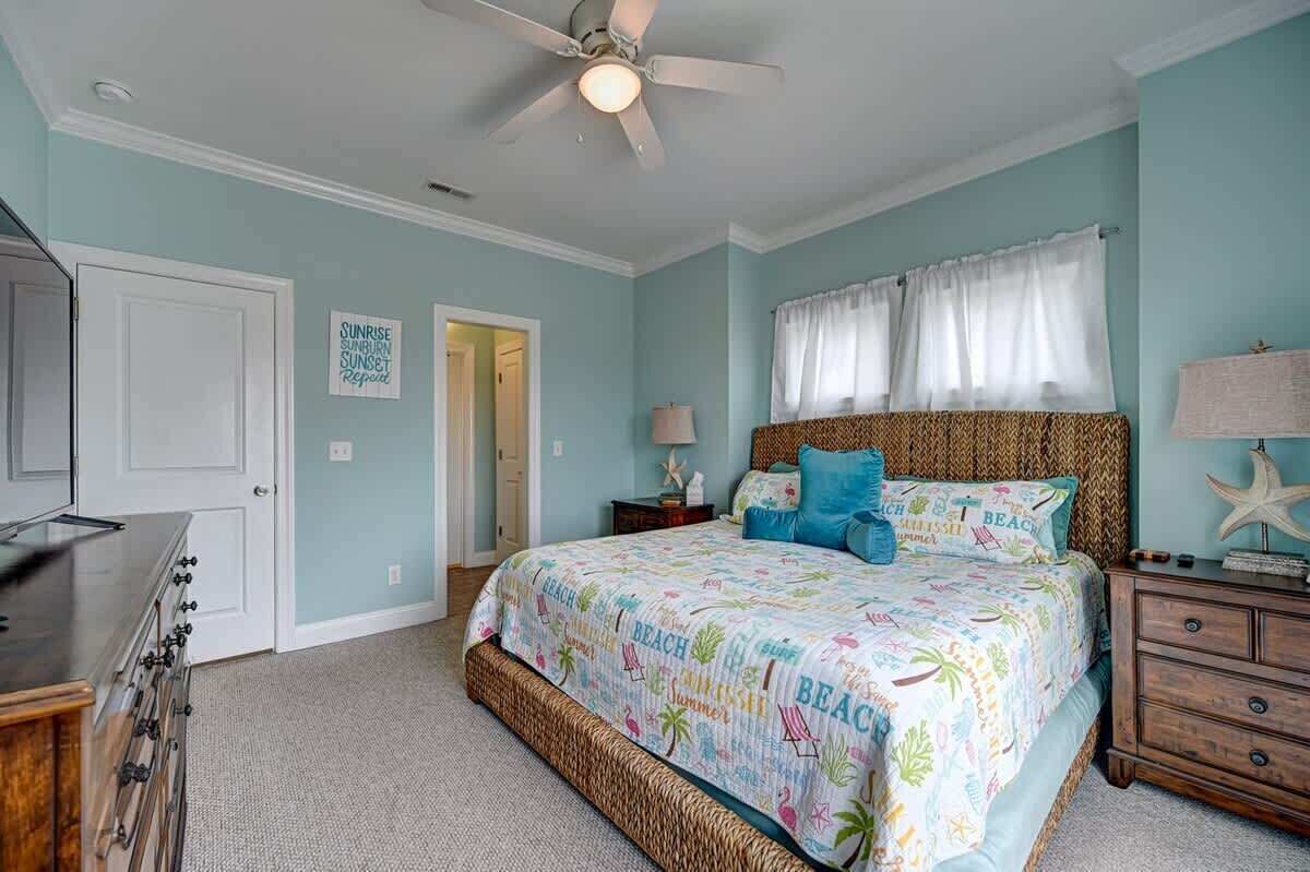 A bedroom with a bed, a ceiling fan, a dresser, and a nightstand.