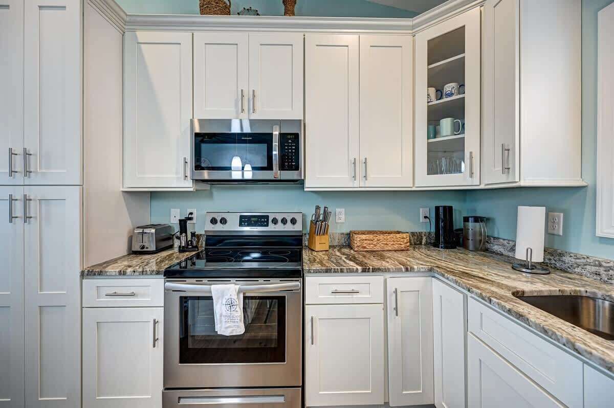 A kitchen with white cabinets, a microwave, a stove, and a sink.