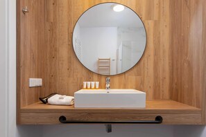 A bathroom with a wooden vanity, a round mirror, and a white sink. - Mielno | 11 Piastów Street | Modern Apartment | Sea View (Mielno)