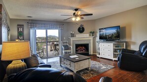 A living room with a fireplace, a television, a ceiling fan, and a view through a glass door. - FREE Dollywood Ticket • Whispering Pines 143 • 2bd/2ba • City View • Pools (Pigeon Forge)