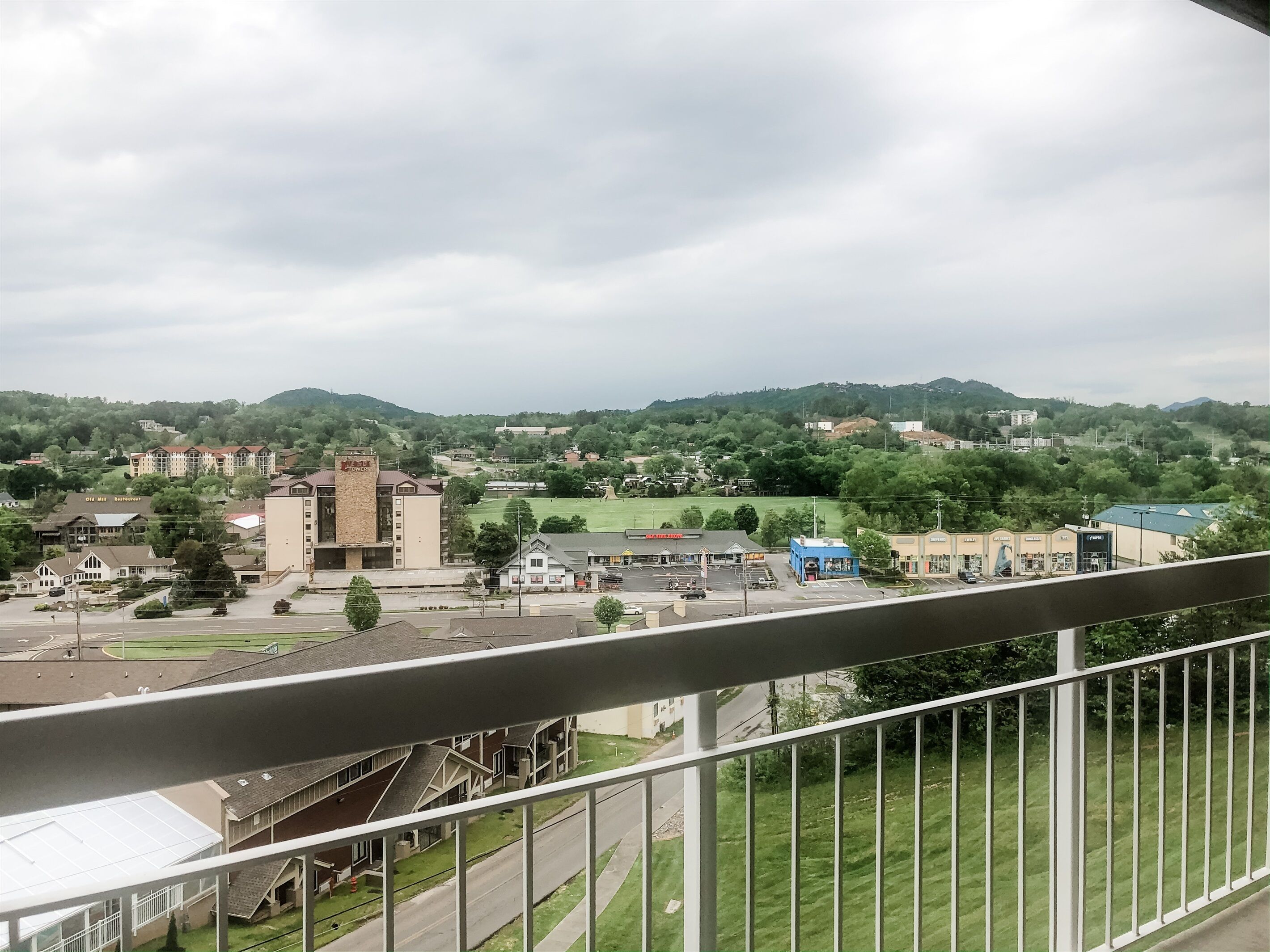 A view of a town with buildings, a road, and green hills in the background.