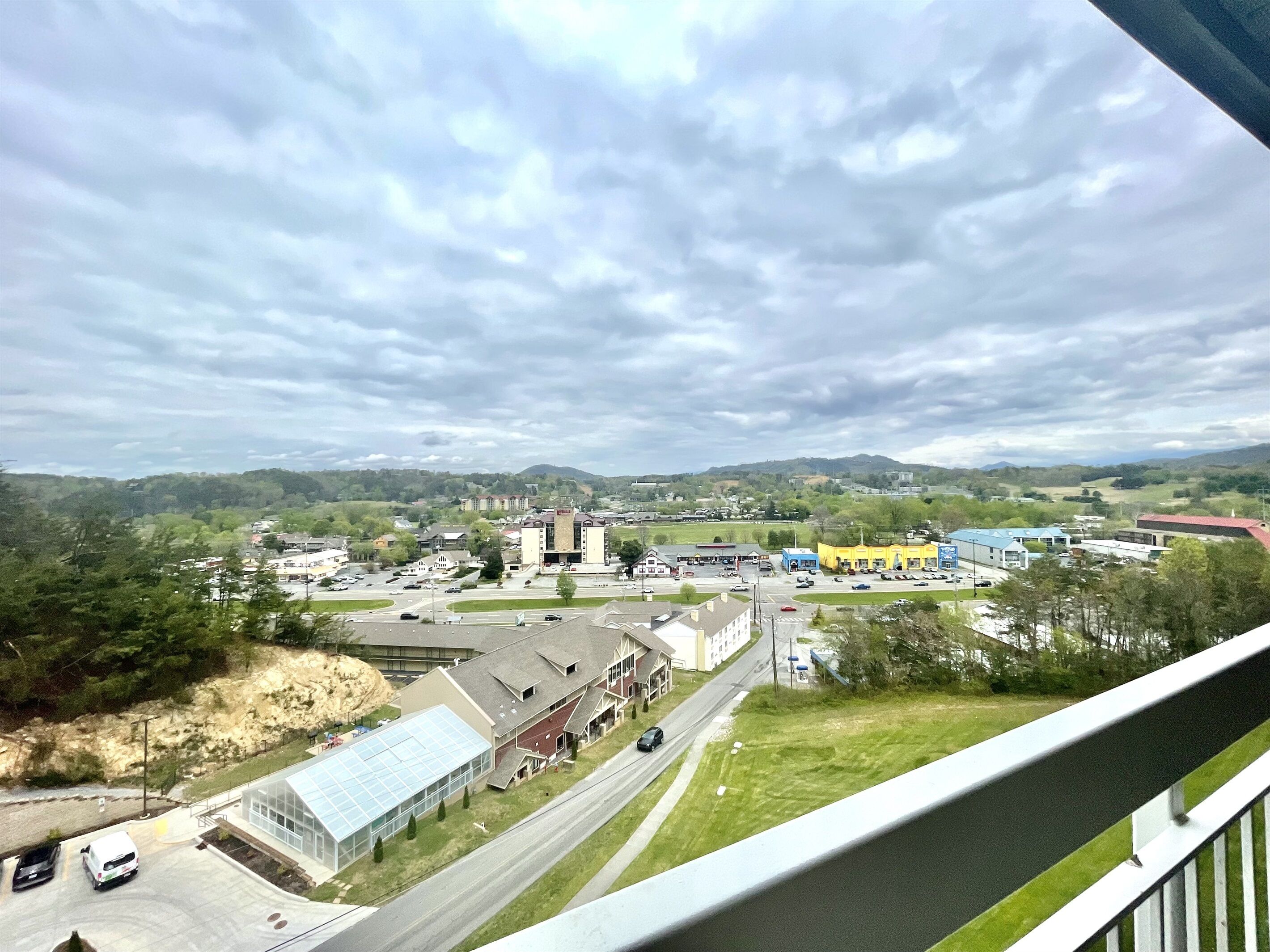 A town with a mix of commercial and residential buildings, a large parking lot, and a view of distant hills.